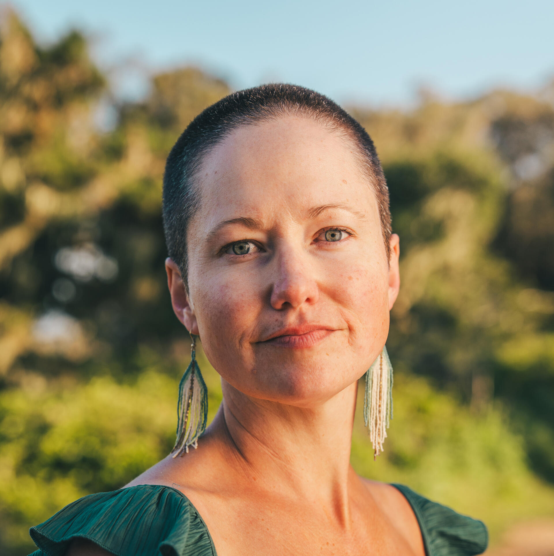 Melissa Bullock headshot Woman with a shaved head and dangly earrings smiling